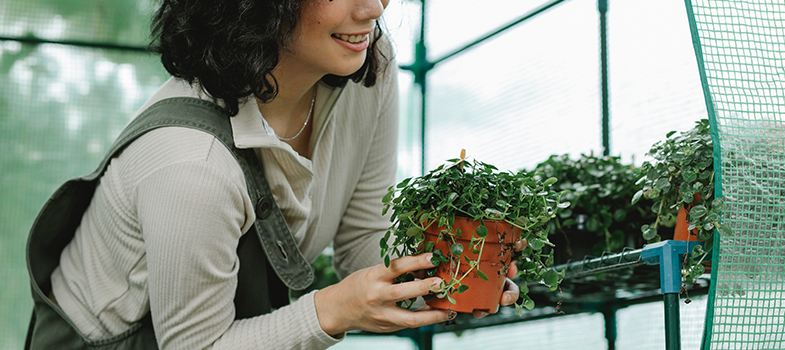 Woman holding a potted plant and smiling at it.