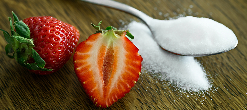 Teaspoon of sugar kept beside strawberries.